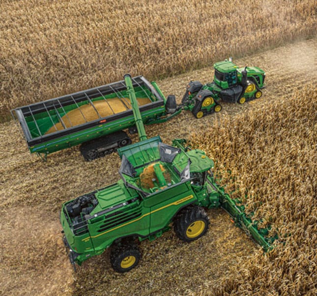 Combine unloading harvested corn into a grain cart pulled by a tractor in a cornfield.