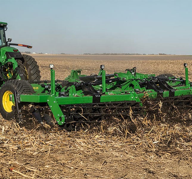 deere tractor plows through a field using a large implement to break up soil and residue.