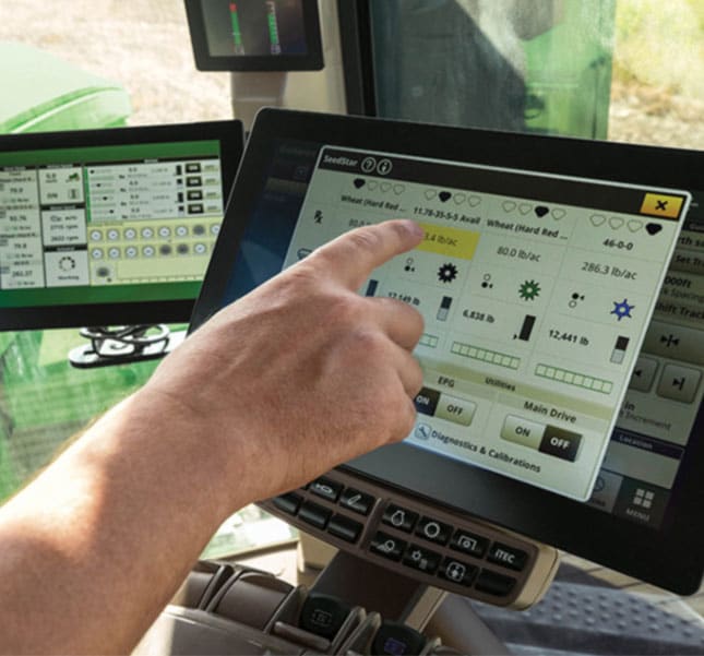 Hand touching a touchscreen display with precision agriculture controls inside a tractor cab.