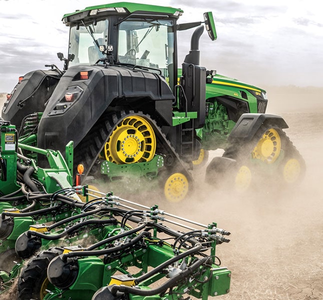Tracked tractor pulling field equipment through dry soil.