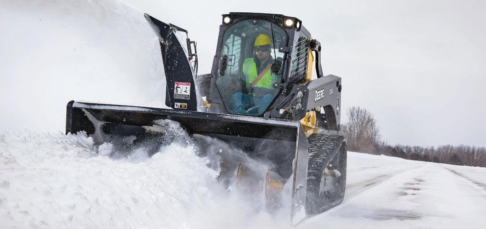 John Deere skid steer with snow blower attachment moving snow.