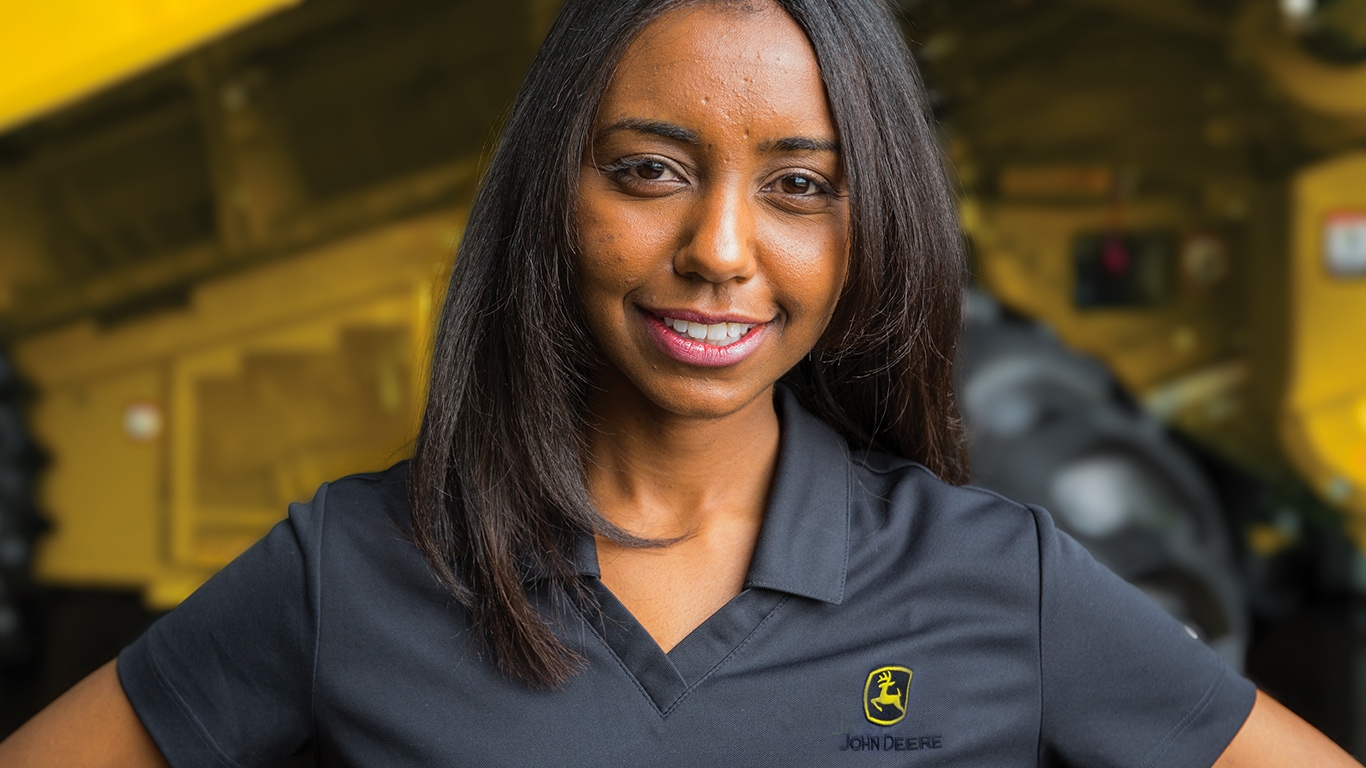 a woman wearing a black John Deere shirt smiling in front of construction equipment
