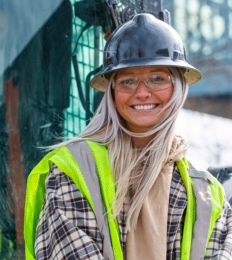 Female operator Taylor Jones standing in front of the 324G Skid Steer