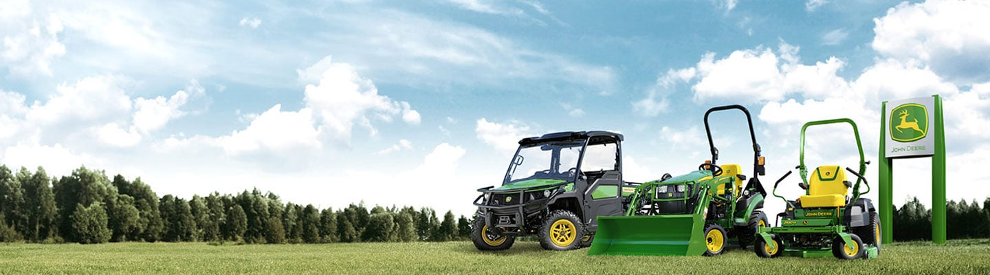 Gator(TM) XUV835M, 1025R compact tractor and Z530M Zero-turn mower parked in a field in front of John Deere dealer signage