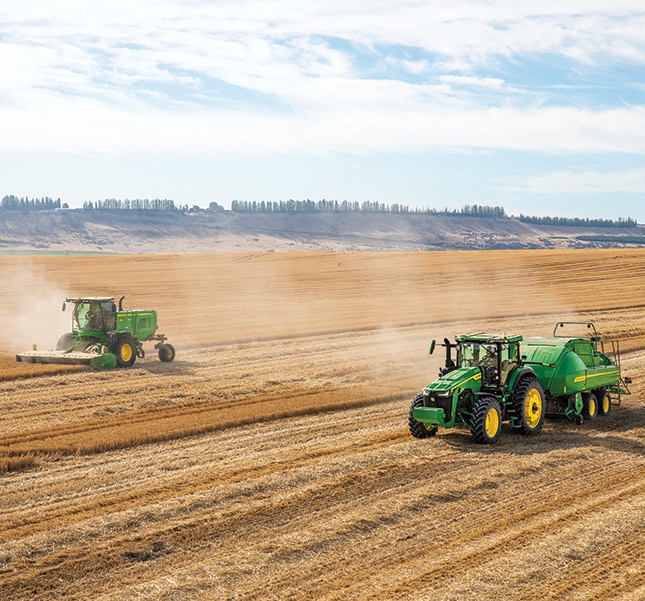 A windrower, tractor and a baler in a field.