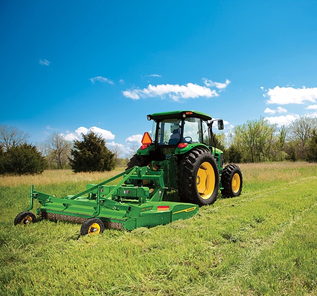 A green tractor pulling a rotary cutter