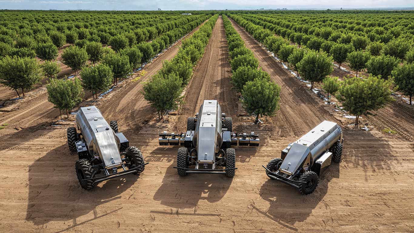 Three GUSS sprayers with orchard in background