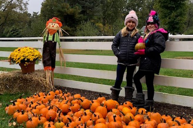 Photo of two young girls posing in front of a pile of pumpkins