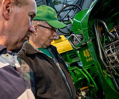 Two older gentleman examine a vintage John Deere Tractor