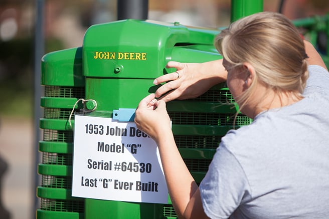 Woman attaching a piece of paper with the 1953 John Deere Model G tractor details