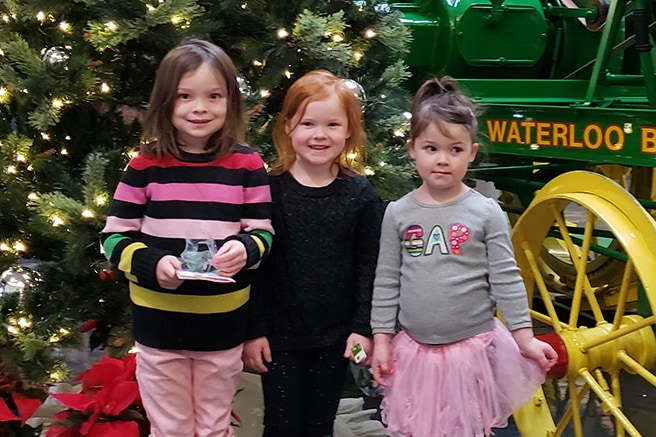 Three young girls standing in front of the Christmas tree next to a Waterloo Boy tractor