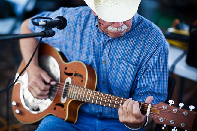 Older man with cowboy hat playing on a guitar outdoors