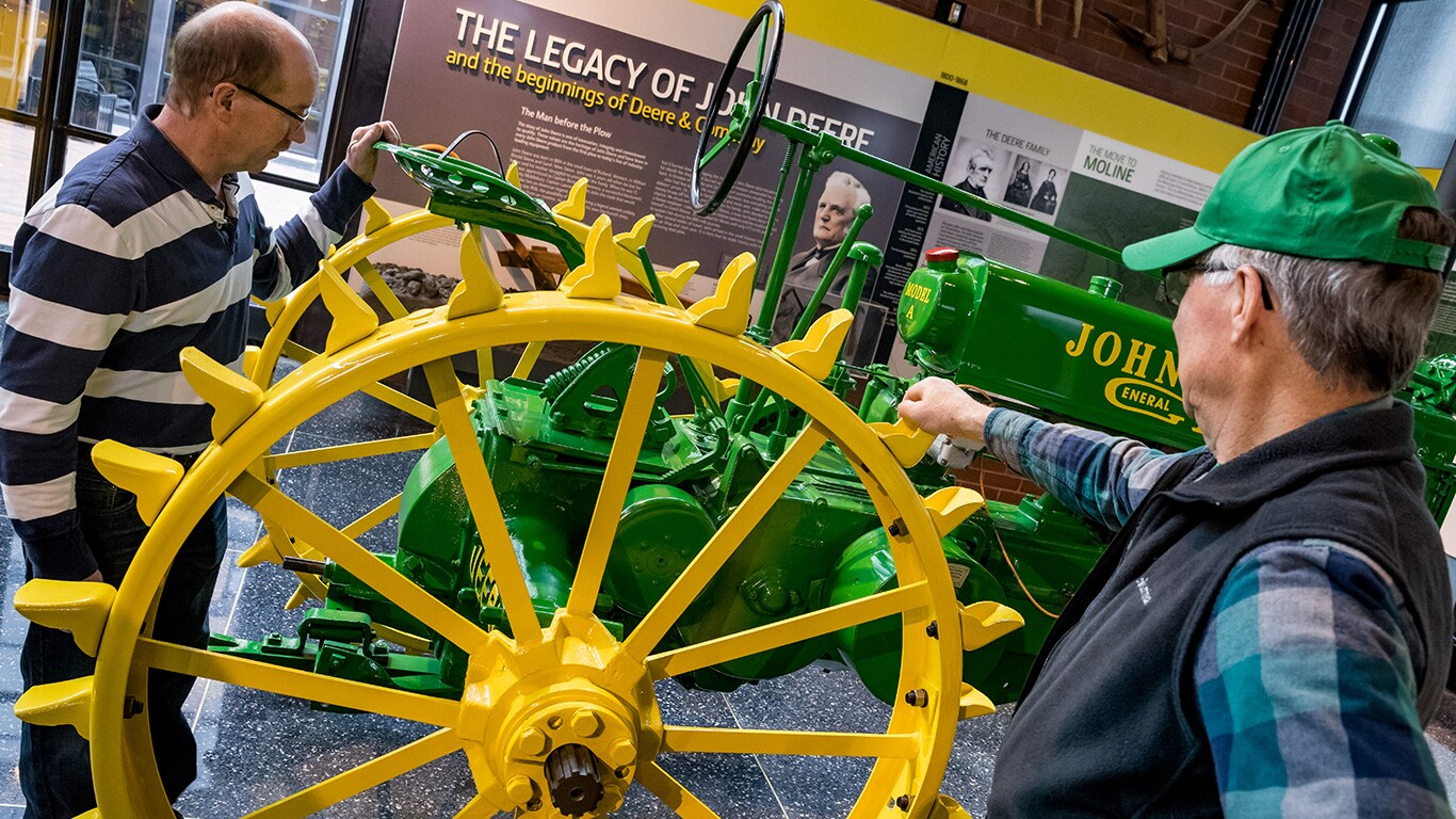 Two older gentleman examine a vintage John Deere Tractor