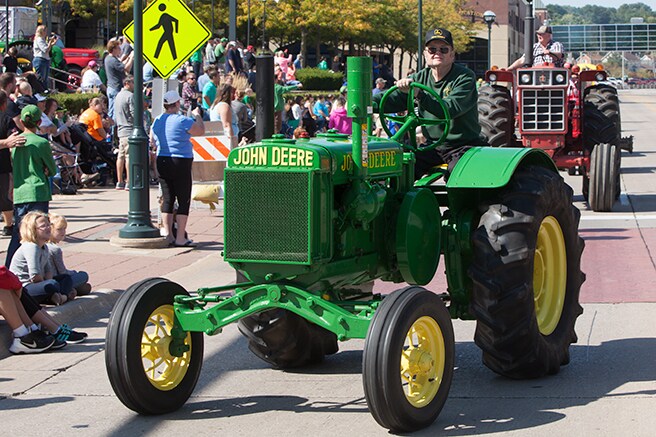 Two heritage tractors driving by the parade crowd in front of the Pavilion