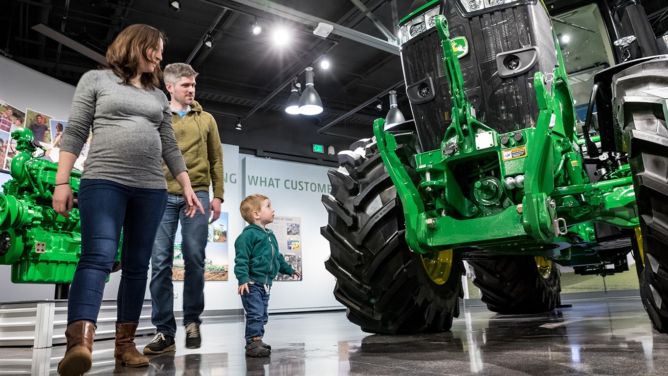 A boy walking around a large tractor with mom and dad