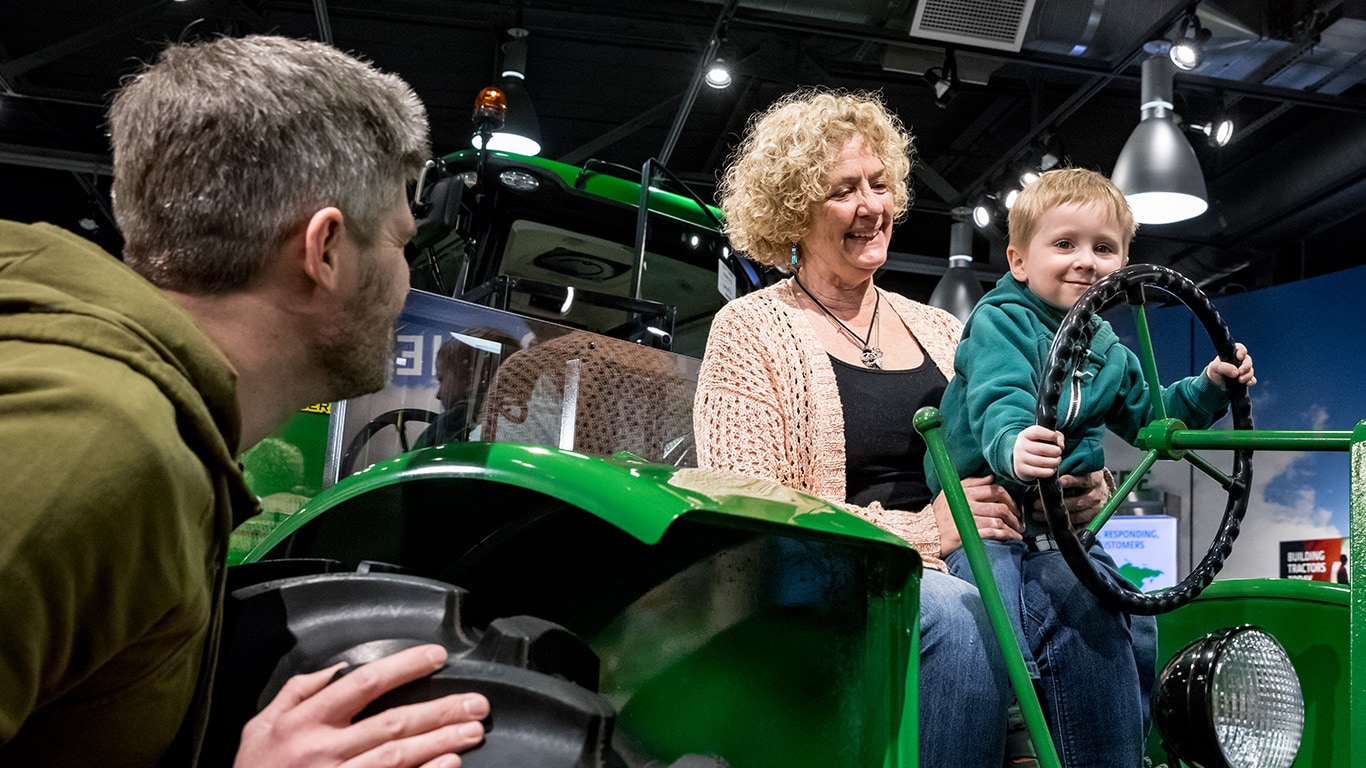 Father looking on as boy sits on grandma’s lap on a vintage tractor