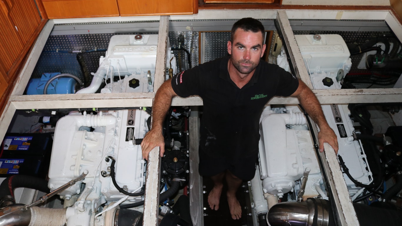 Brad Belcher standing next to twin John Deere PowerTechTM 6090SFM85 engines in the engine room of his Dyna 53 yacht.