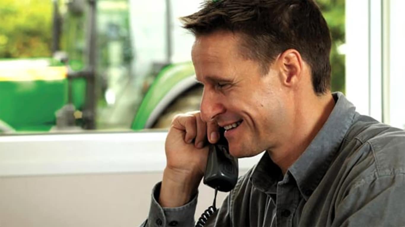 Man talking on the phone in front of a window with a tractor in the background