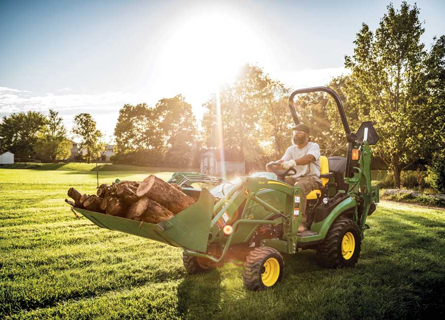 Side view of a John Deere Compact Tractor with fork attachments moving a hay barrel