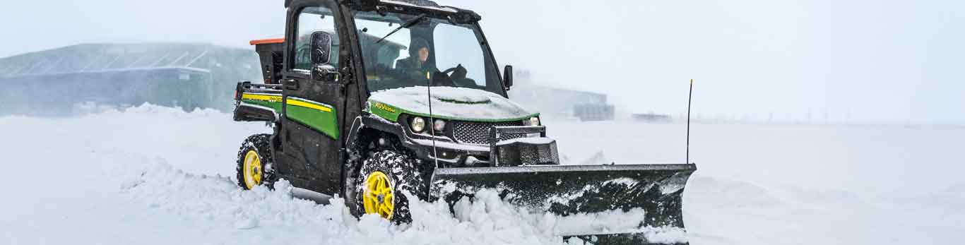 Woman driving a John Deere XUV835M Gator Utility Vehicle with snow blade plowing through the snow