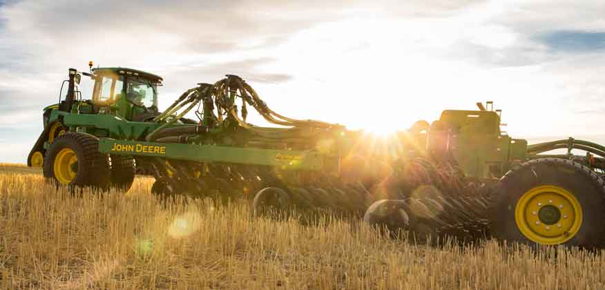 John Deere Tractor with harvesting equipment working in a field with the sun peeking through