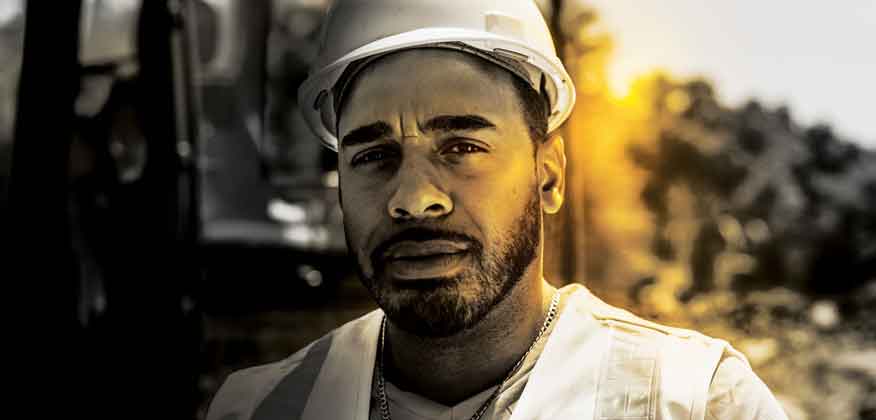 Man standing at a worksite with a hard hat and John Deere Construction equipment in the background