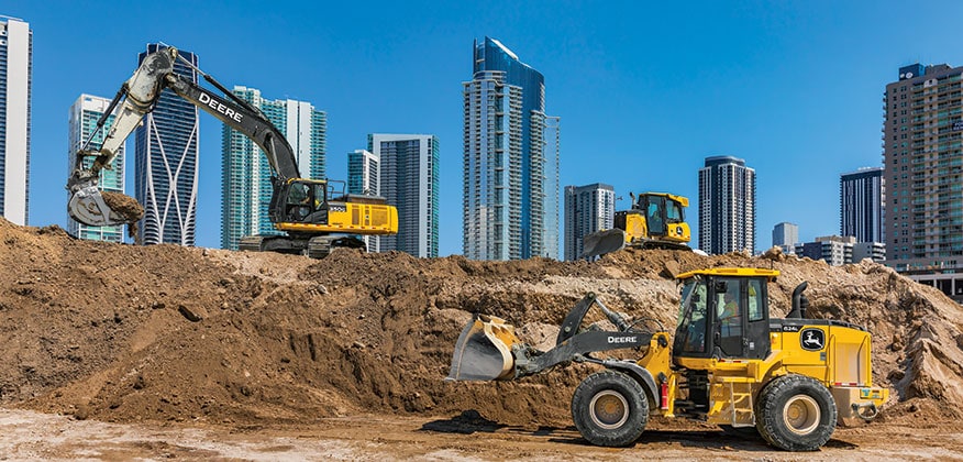 John Deere construction equipment working in front of city landscape