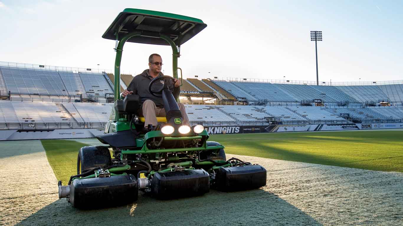 Man operating a John Deere sports turf equipment on a football staium field