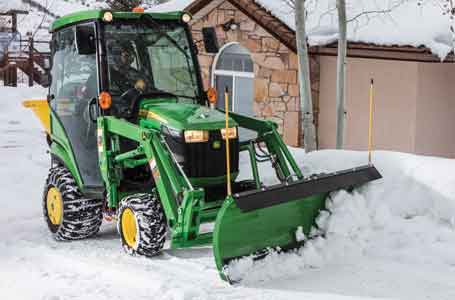 John Deere Compact Tractor with cab and slow plow attachment pushing snow