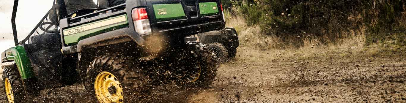 Two people in a John Deere XUV825M Gator Utility Vehicle riding through a trail