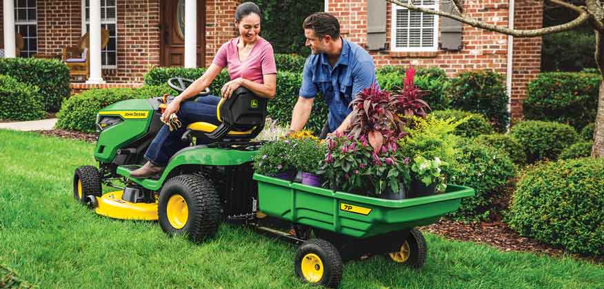 Couple landscaping front yard using a John&bsp;Deere lawn tractor and cart attachment to haul plants