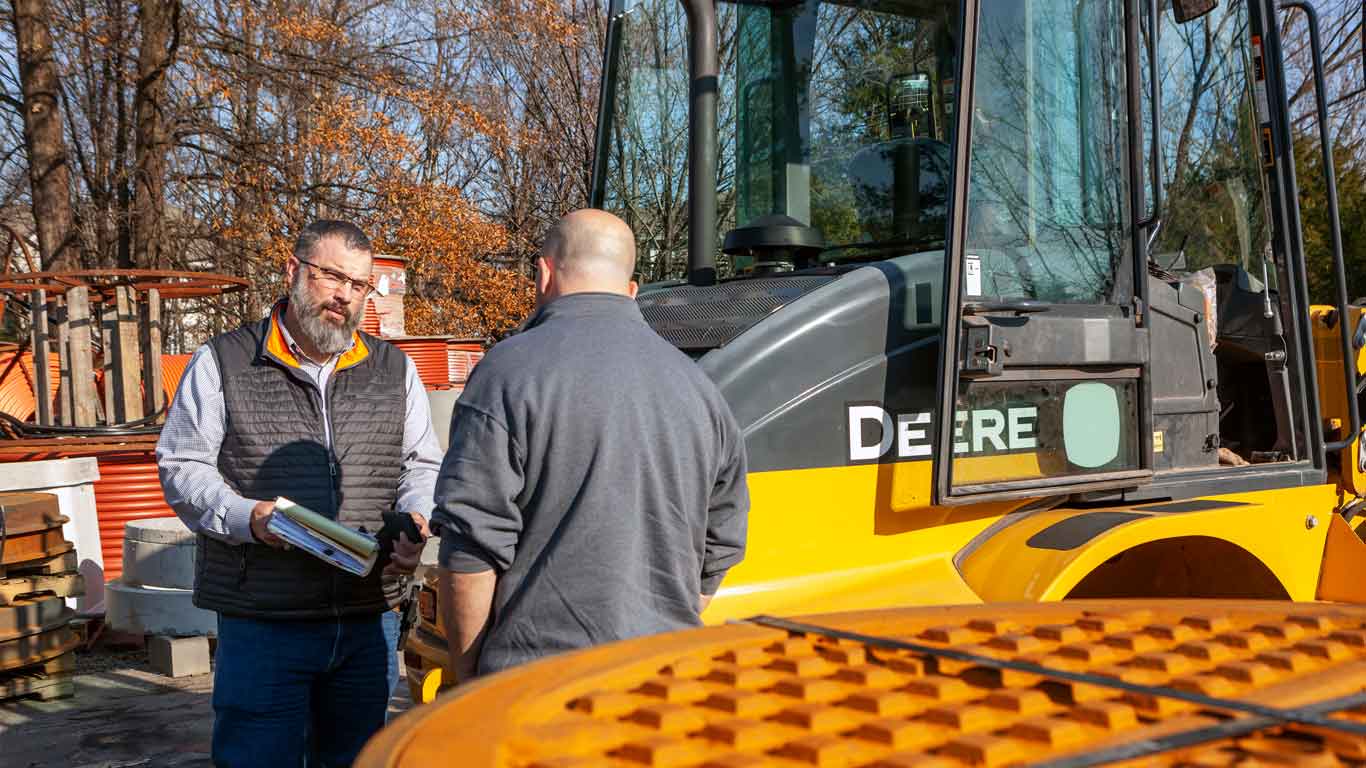 Two people at a dealership with John Deere Construction equipmenty