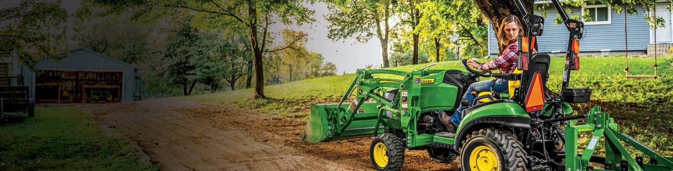 Woman driving a 1025R compact tractor with loader and box blade levelling her driveway