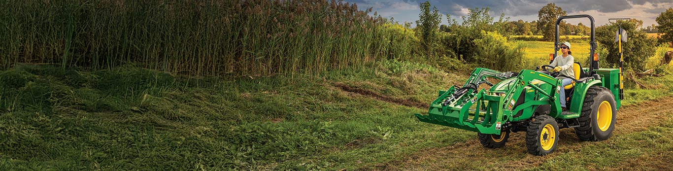 Woman driving a 3E Series Compact Tractor next to a field.