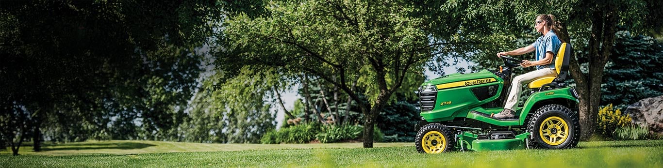  A woman mowing the lawn with an open station John Deere X739 lawn tractor.