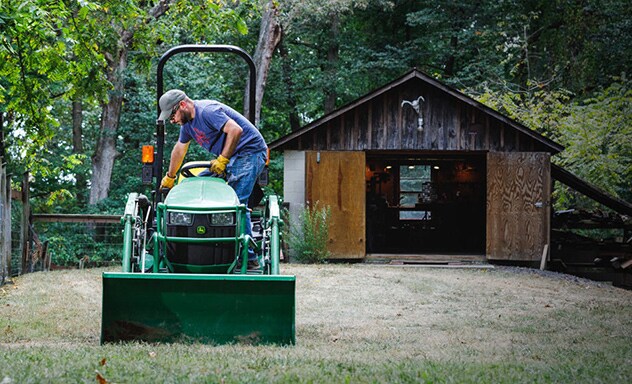  Man climbing on to a 1023E Sub-Compact Tractor with a loader attached.