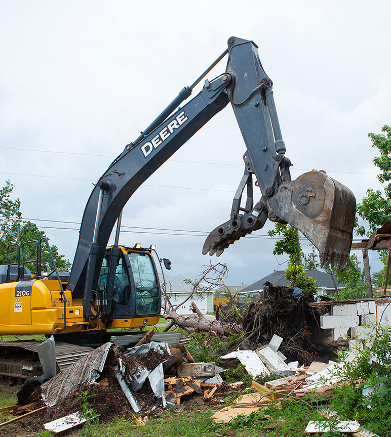 210G Excavator drops a load of rubble from its bucket with claw while cleaning up around a building severely damaged from a hurricane