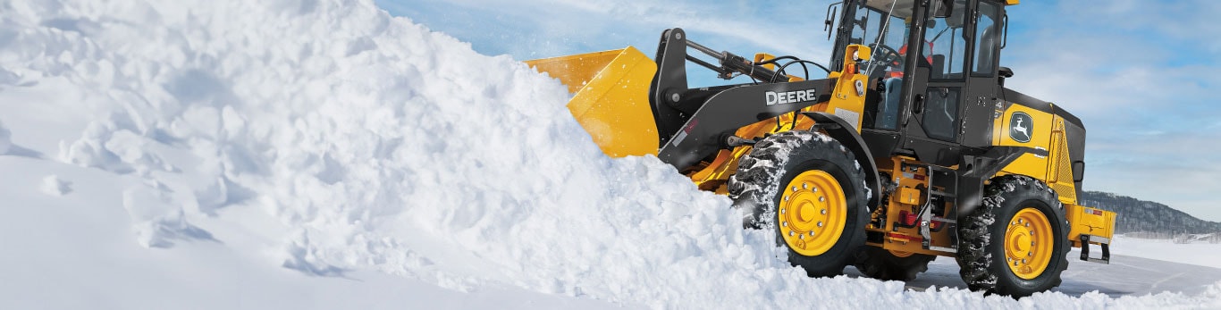 A 444G Wheel Loader with snowblade attachment plowing snow in front of a blue sky. 
