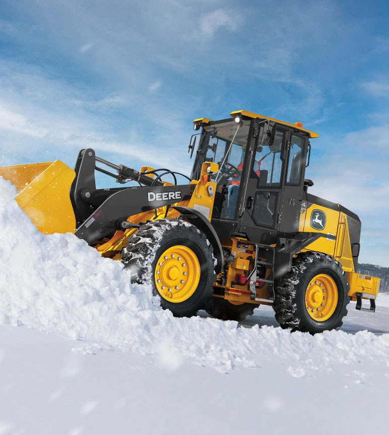 A 444G Wheel Loader with snowblade attachment plowing snow in front of a blue sky.