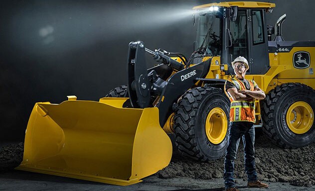 An operator stands proud with arms crossed in front of a 644L Wheel Loader parked on a pile of dirt
