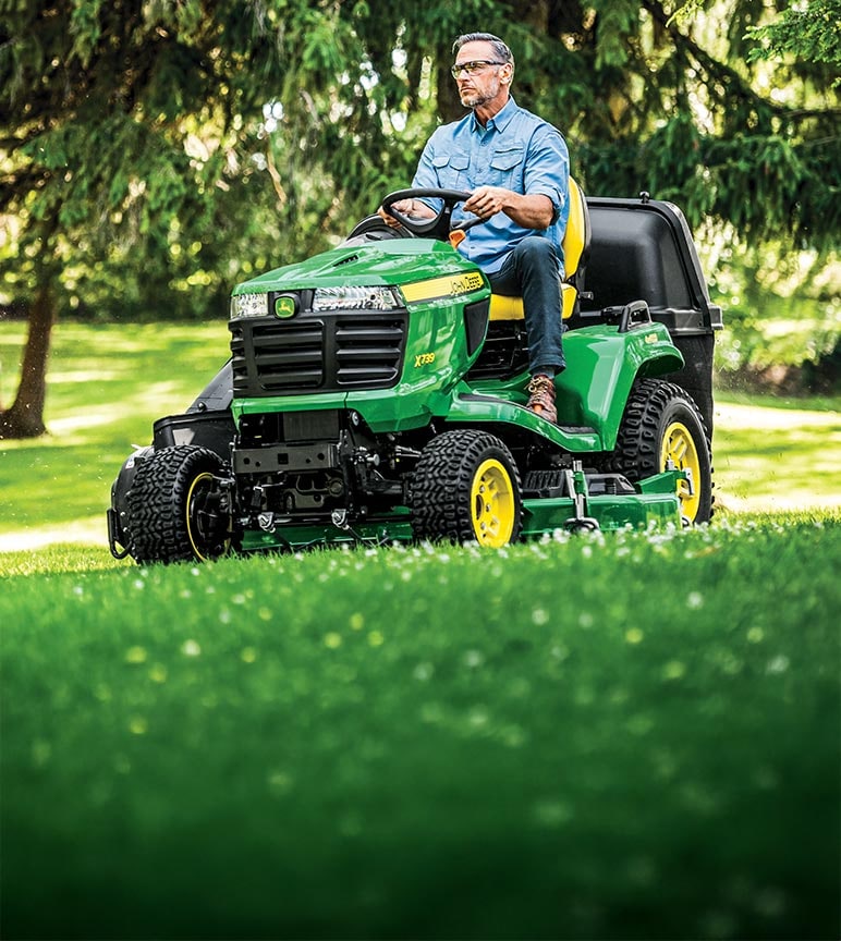 A man mowing the lawn with an open station John Deere X739 lawn tractor.