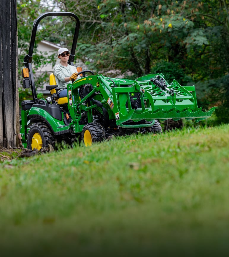 Woman driving a 1025 Compact Tractor up a slight hill.