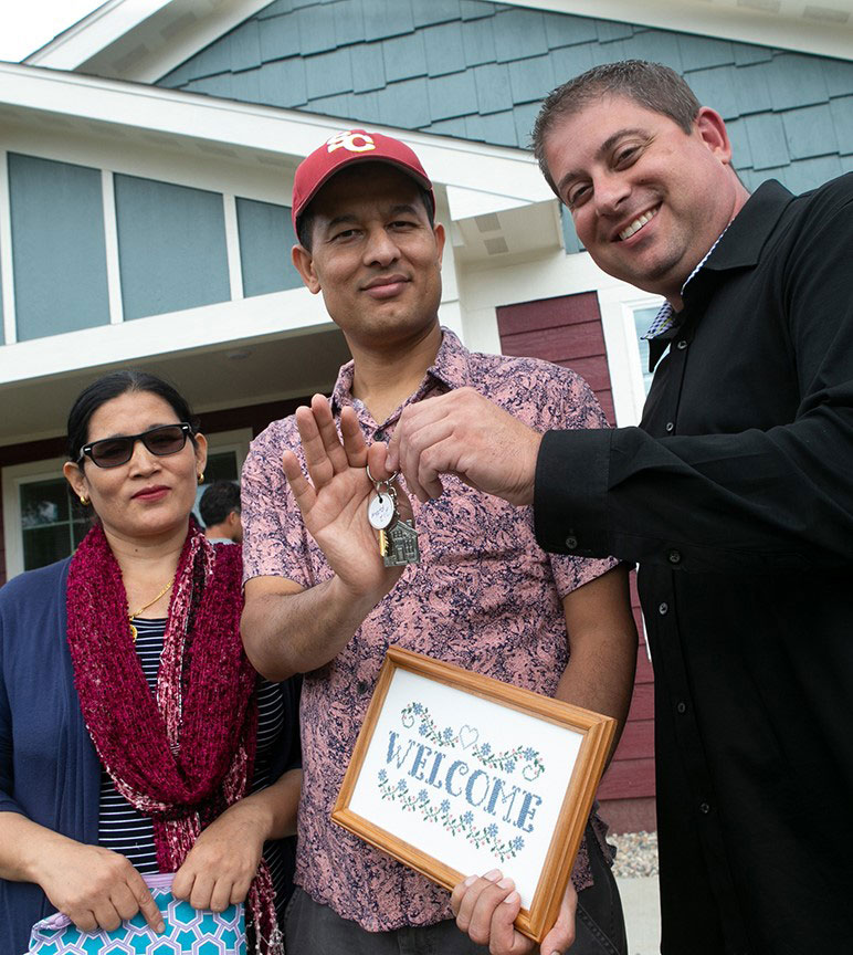 Man handing keys to couple standing in front of their new house