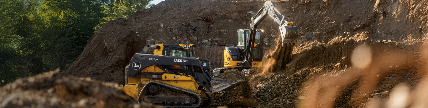 Compact track loader and compact excavator digging up dirt