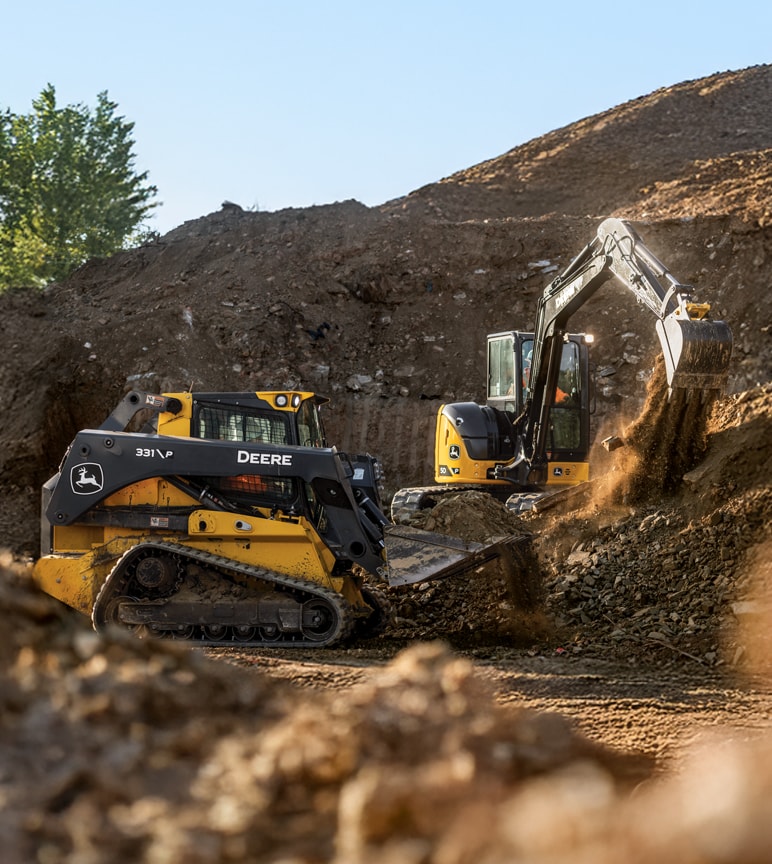 Compact track loader and compact excavator digging up dirt