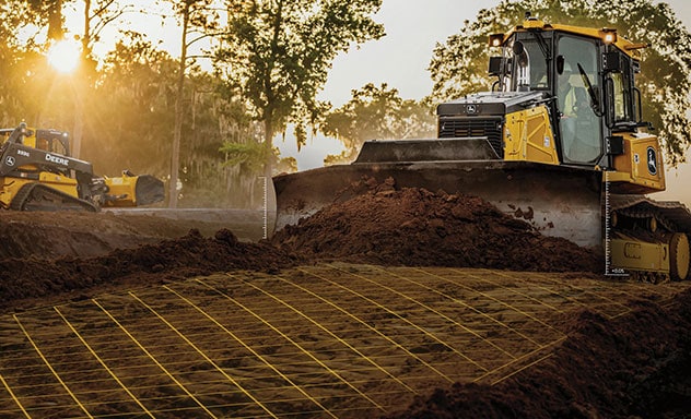 John Deere ADT leveling dirt on worksite while 333G Skid Steer works in back. A yellow grid overlay illustrates the precision construction software.