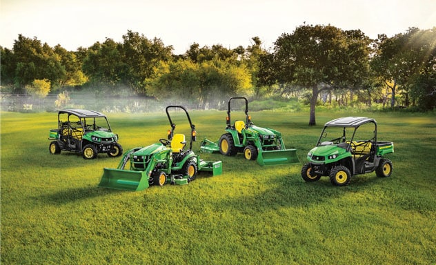 Four John Deere products in a green field with trees and fog in background.