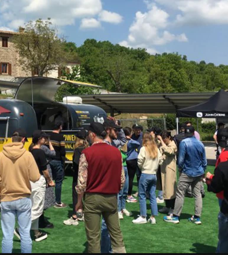 A crowd standing and awaiting food at a black and yellow food truck with tents around.