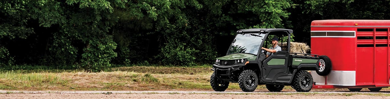 Man driving a Gator XUV with a trailer attached.