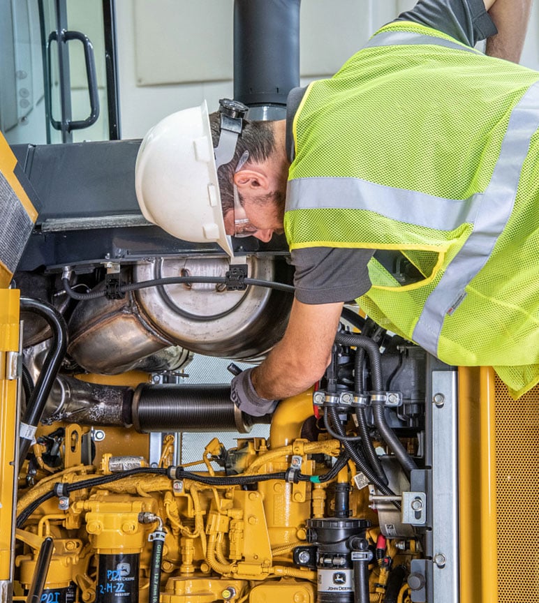 Man with a white hard hat on working on a John Deere with a engine.